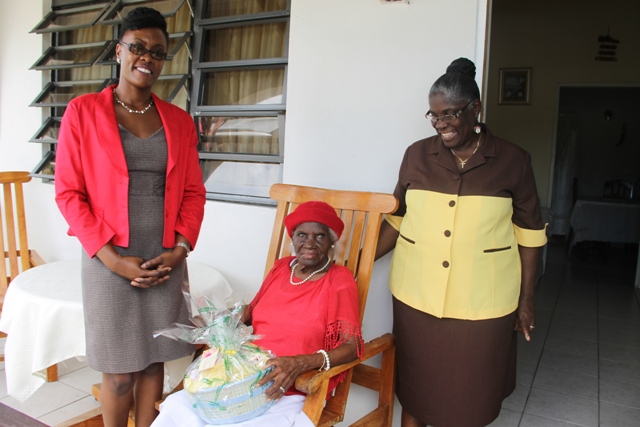 Director of the Nevis Investment Promotion Agency Kimone Moving with Alice Nisbett (seated) and her daughter Muriel St. Jean at Nisbett’s home in Cotton Ground. Nisbett, the oldest person in the St. Thomas’ Parish, was presented with a gift basket from NIPA and the Nevis Financial Services Department on June 17, 2014